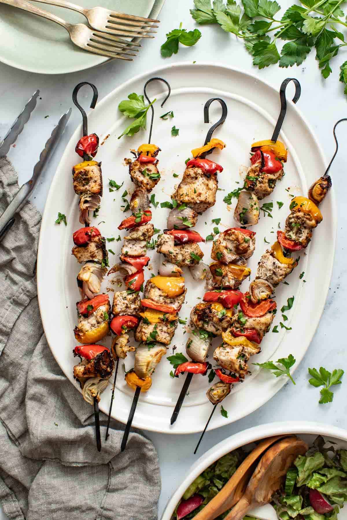 Baked skewers layered with chicken and vegetables, topped with parsley on a white plate.