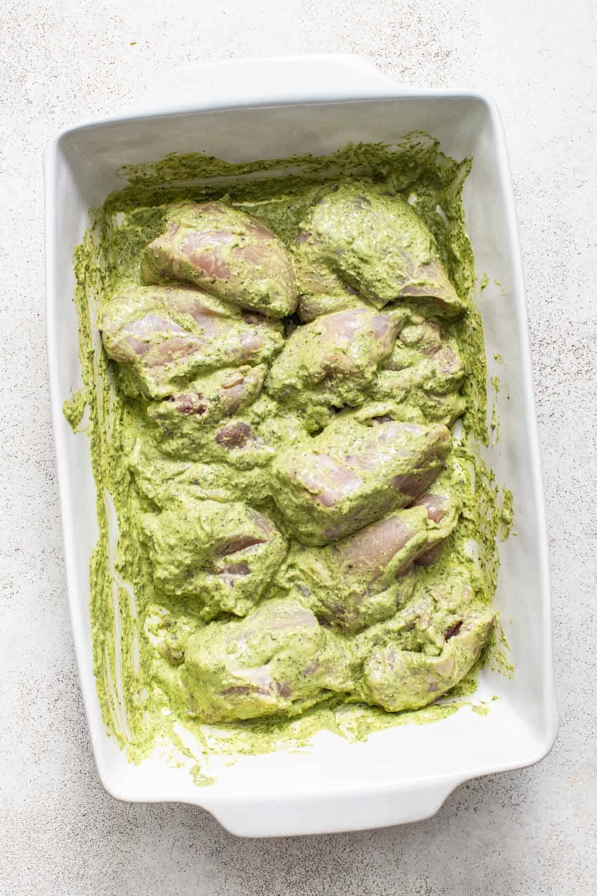 Coating boneless chicken thighs in green goddess marinade sauce.