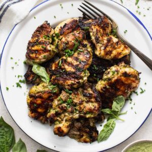 Grilled boneless chicken thighs on a white plate with a fork and basil leaves.