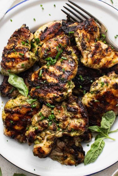 Grilled boneless chicken thighs on a white plate with a fork and basil leaves.