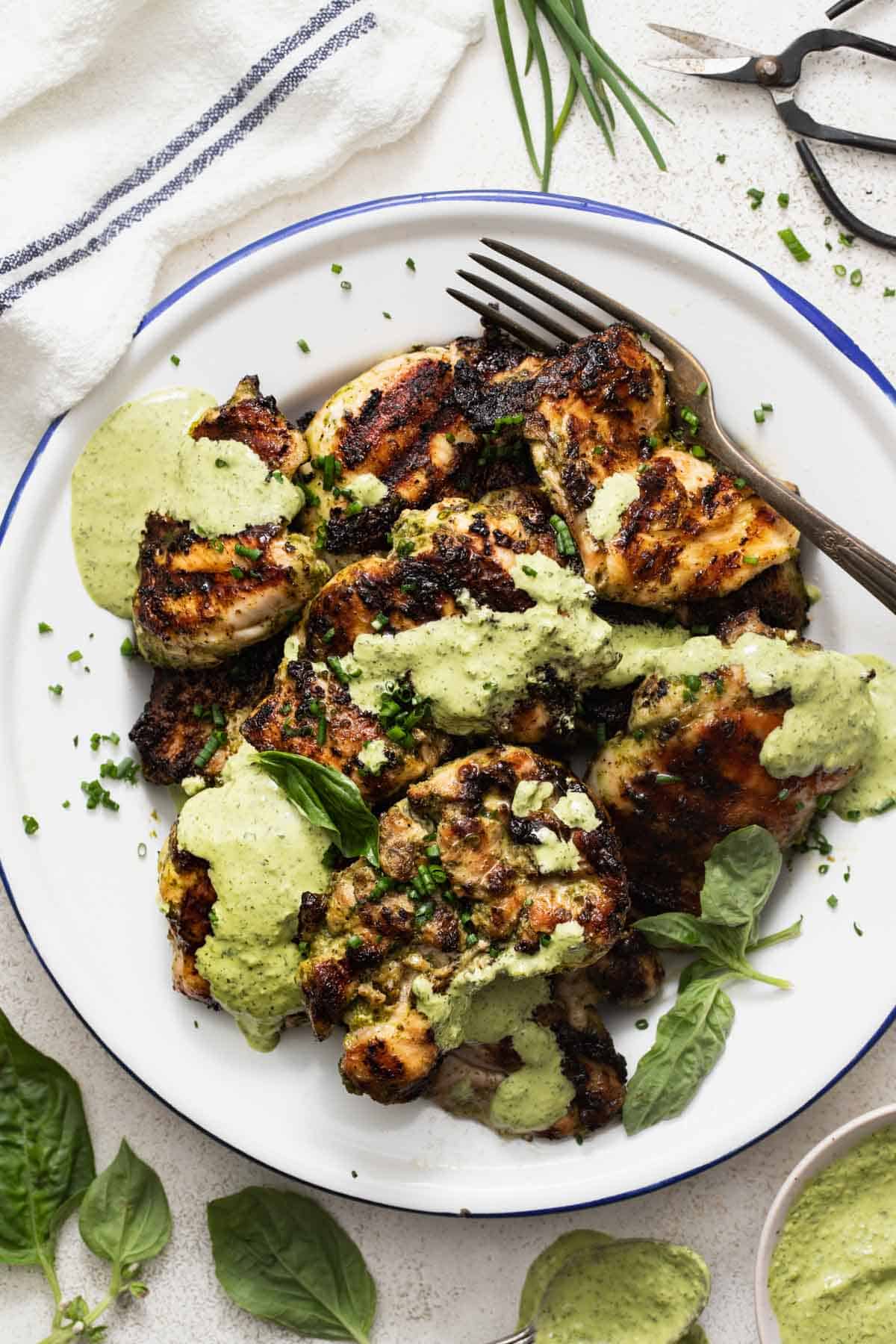 Chicken thighs grilled and drizzled with a green herb sauce on top.