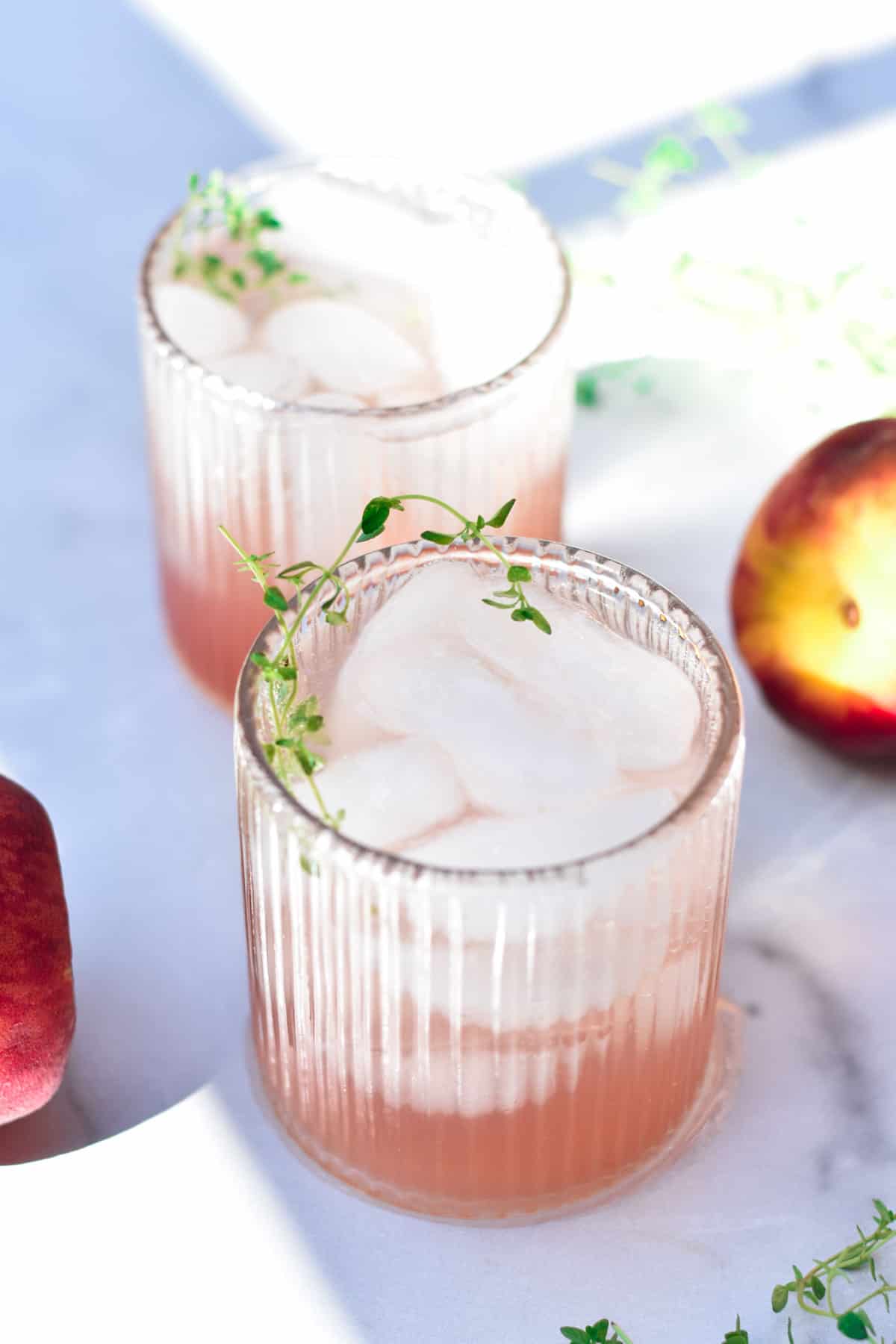 Two peach mocktails next to fresh peaches and fresh thyme.