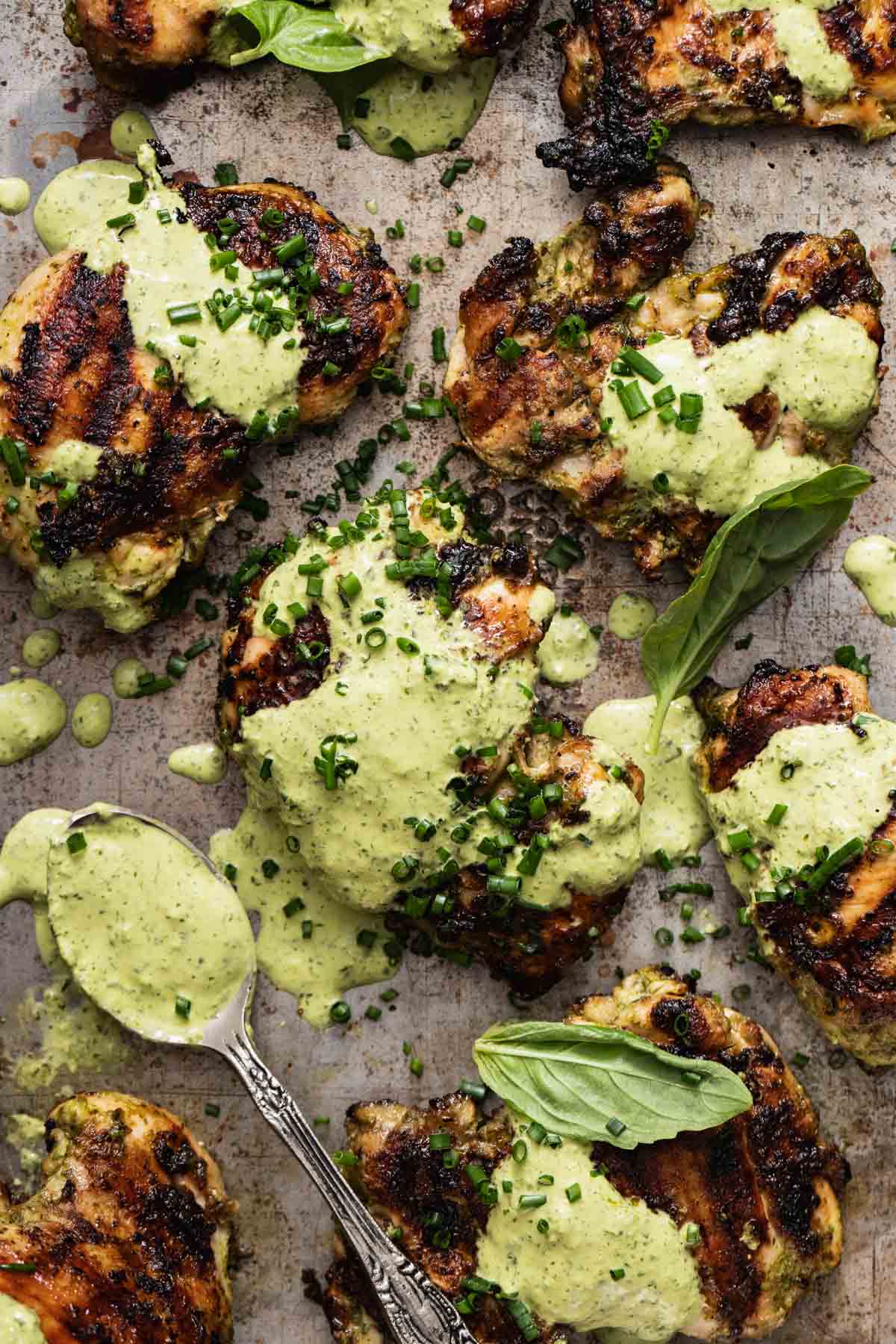 Grilled chicken thighs on a sheet pan coated in a green goddess sauce and chives.