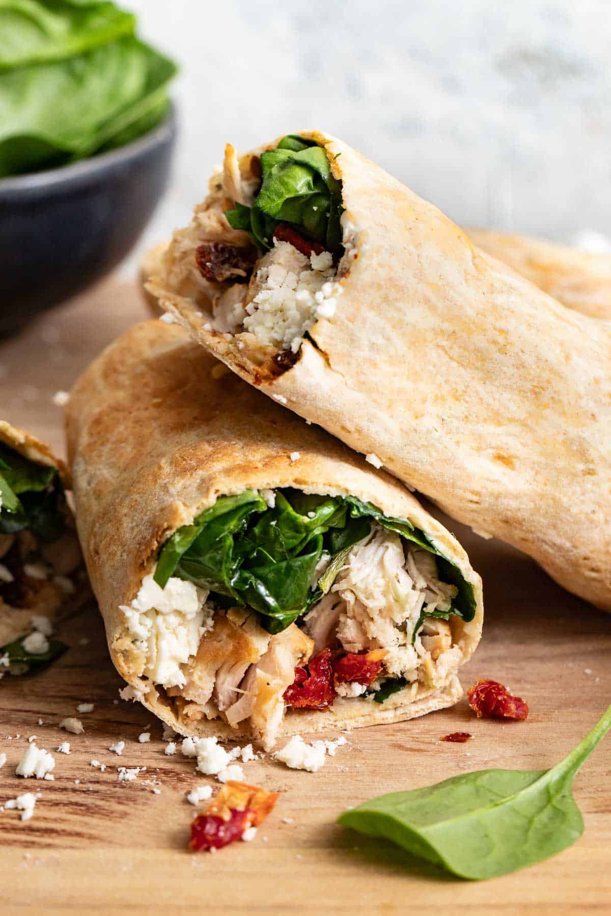 Two chicken wraps stacked on top of a cutting board.