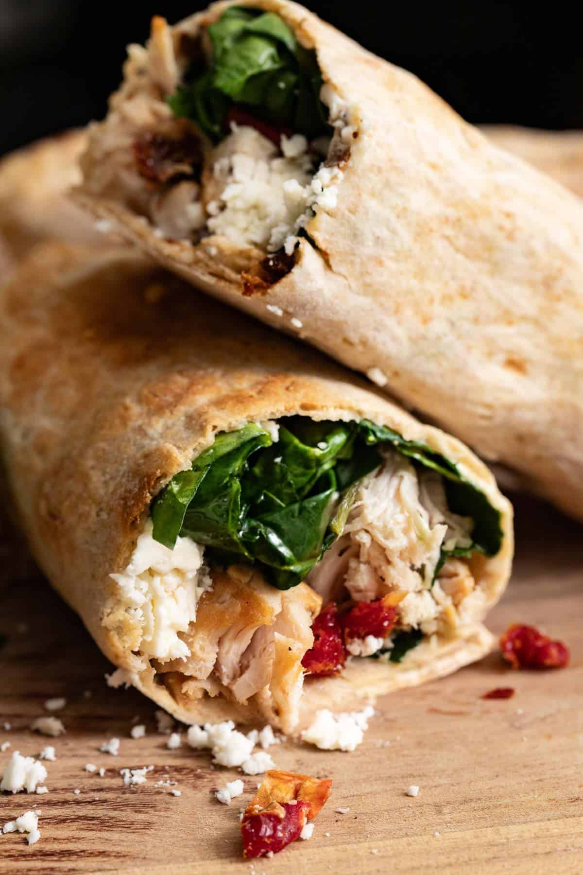 Two wraps stacked on top of a cutting board with feta cheese and chicken. 