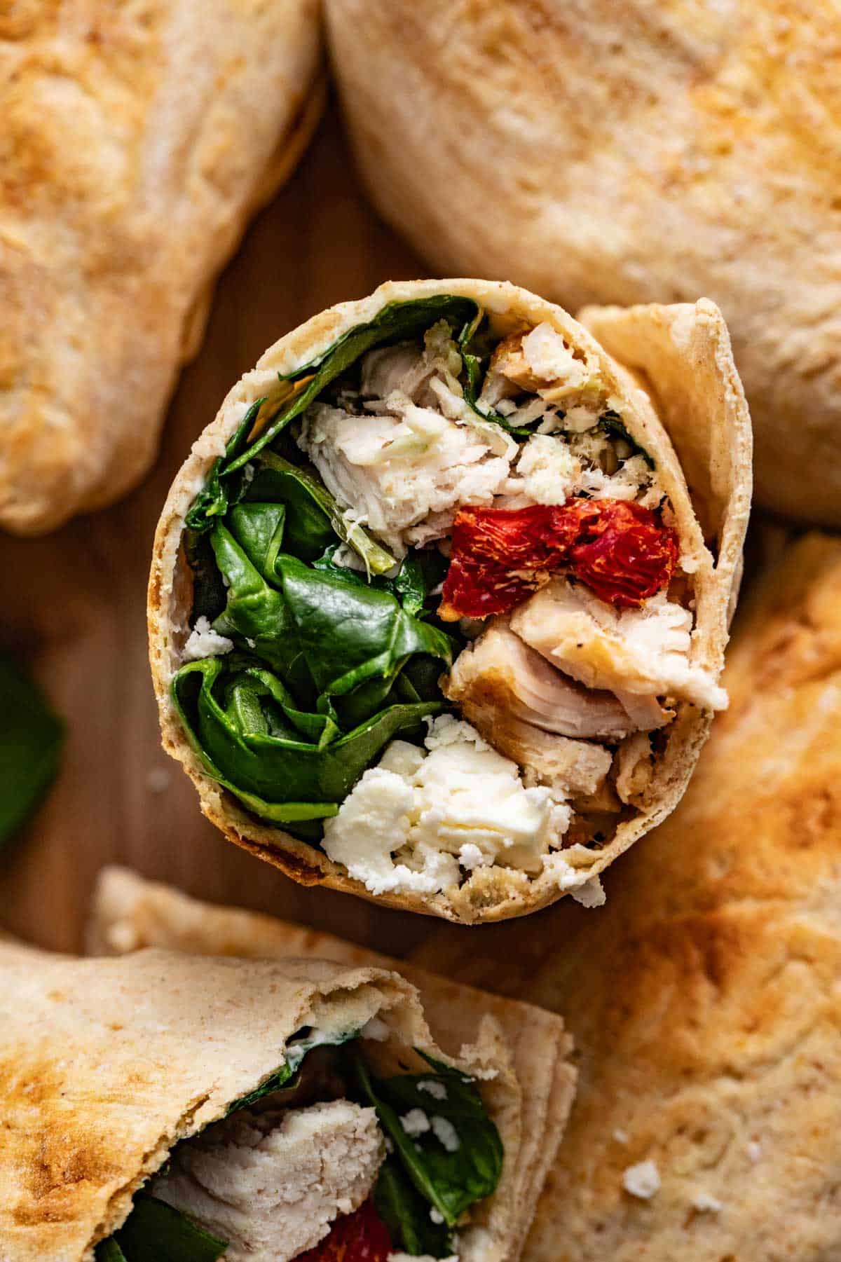 A cut chicken wrap stuffed with spinach, sun-dried tomatoes, grilled chicken, and cheese.