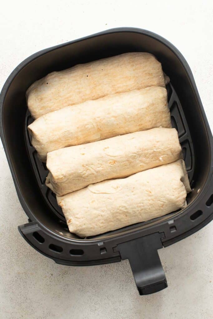 Chicken wraps lined up in an air fryer before frying.