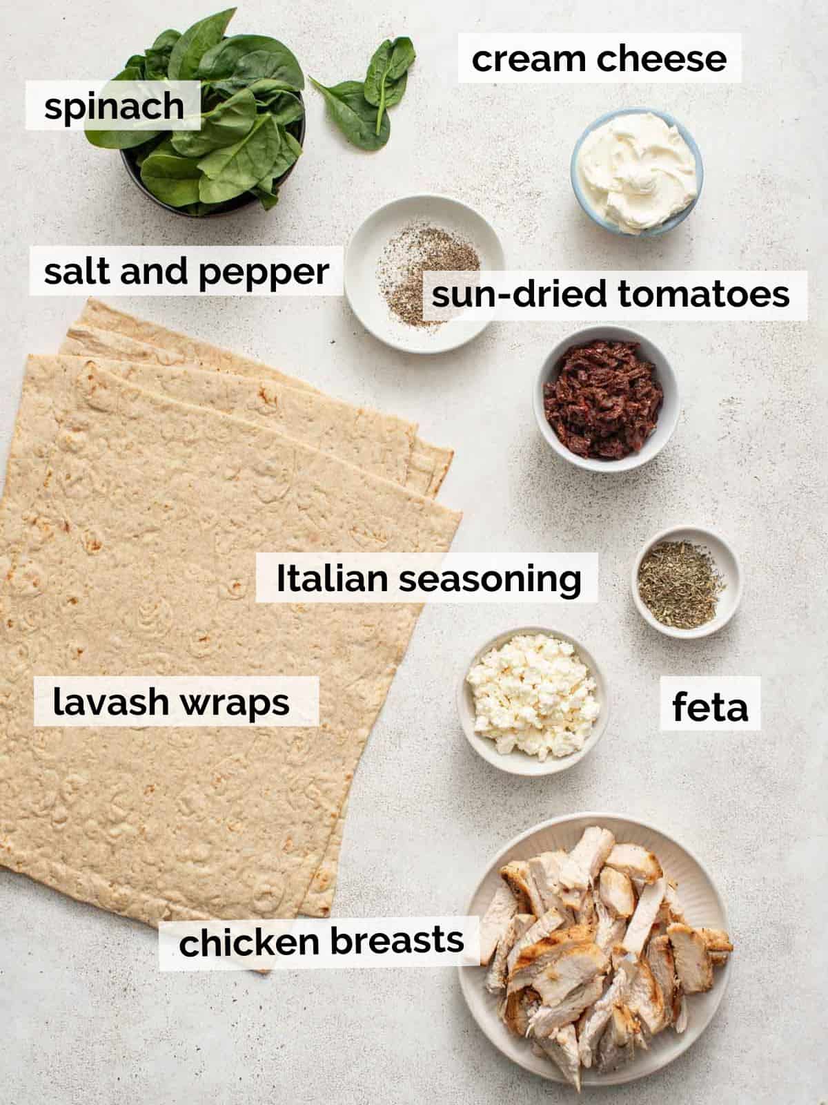 Ingredients for mediterranean chicken wraps on a white table.