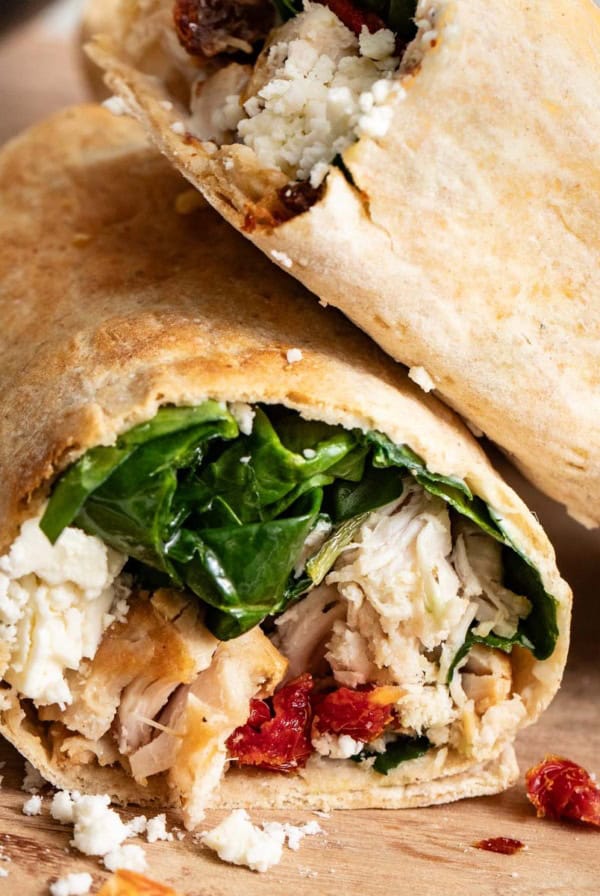 Chicken wraps stacked on top of each other on a cutting board.