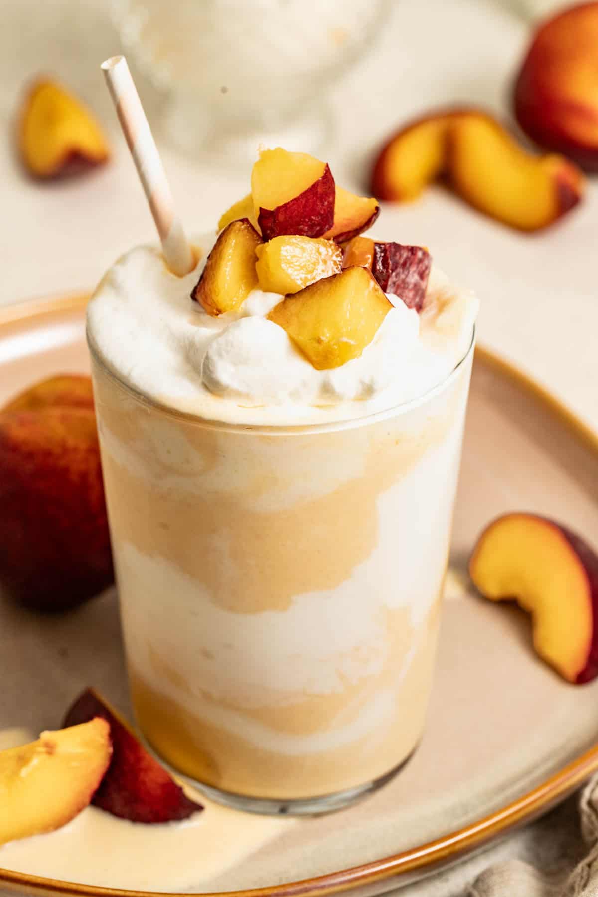 Cream and peaches swirled through a milkshake, on a beige plate with fresh peaches around it.
