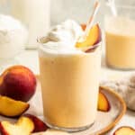 Peach milkshake topped with a peach slice, a straw, and whipped cream.