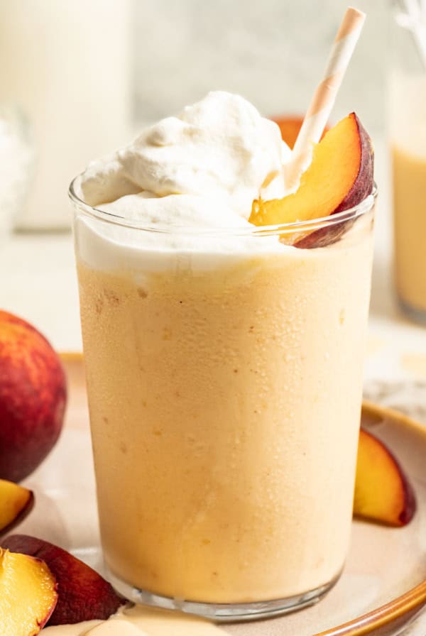 Peach milkshake topped with a peach slice, a straw, and whipped cream.