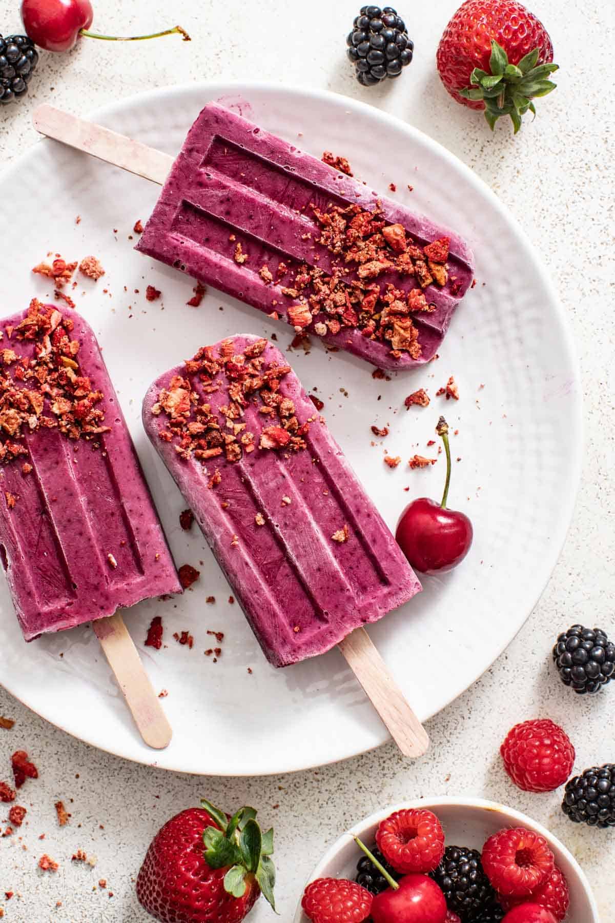 Three berry popsicles coated in crushed strawberries on a white plate.