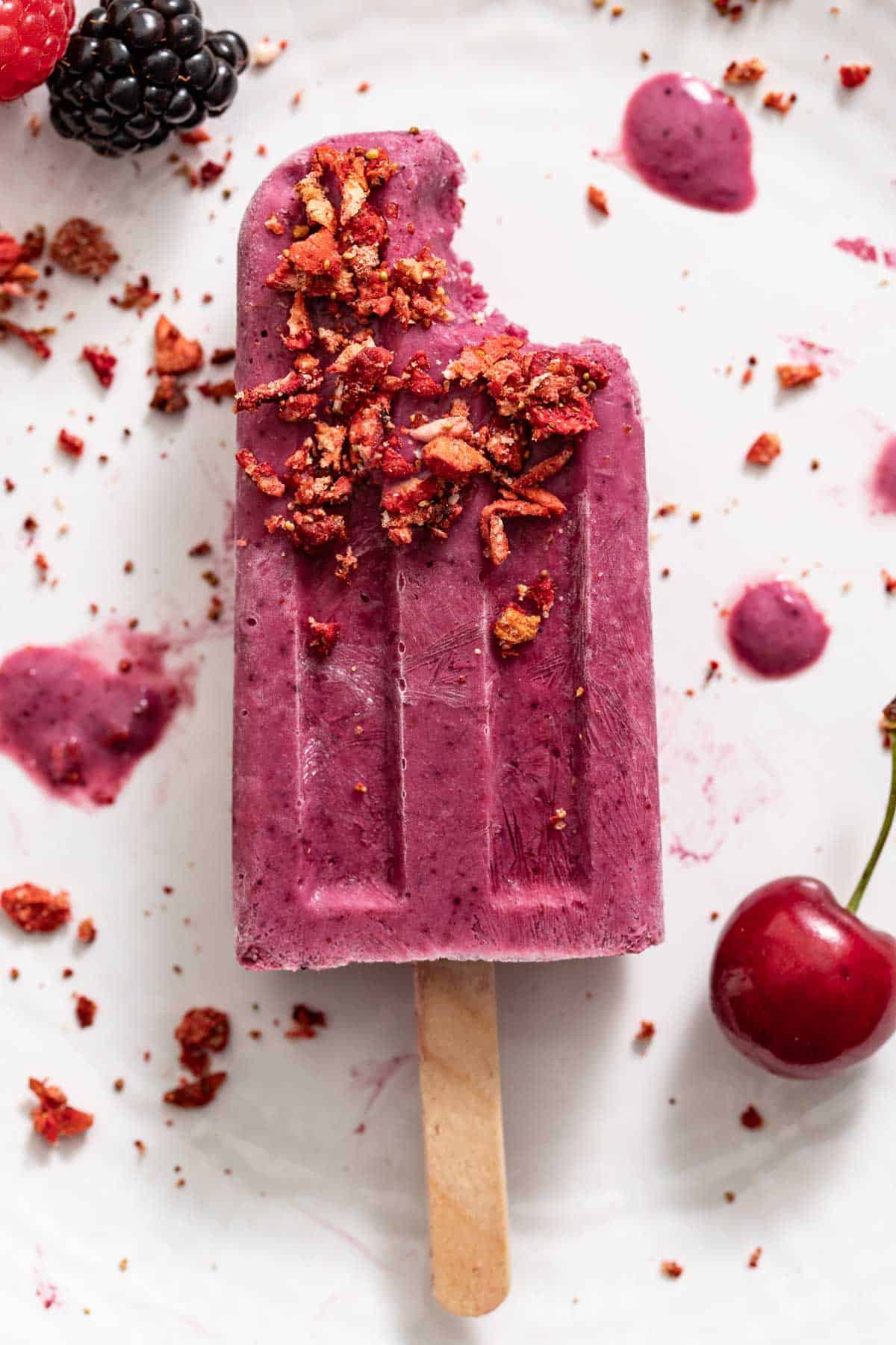 A bite out of a purple popsicle with cherries and blackberries.