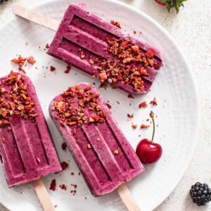 Three berry popsicles coated in crushed strawberries on a white plate.