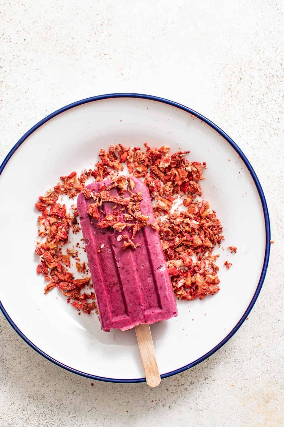 Pressing the popsicle into the crushed freeze-dried strawberries on a plate.