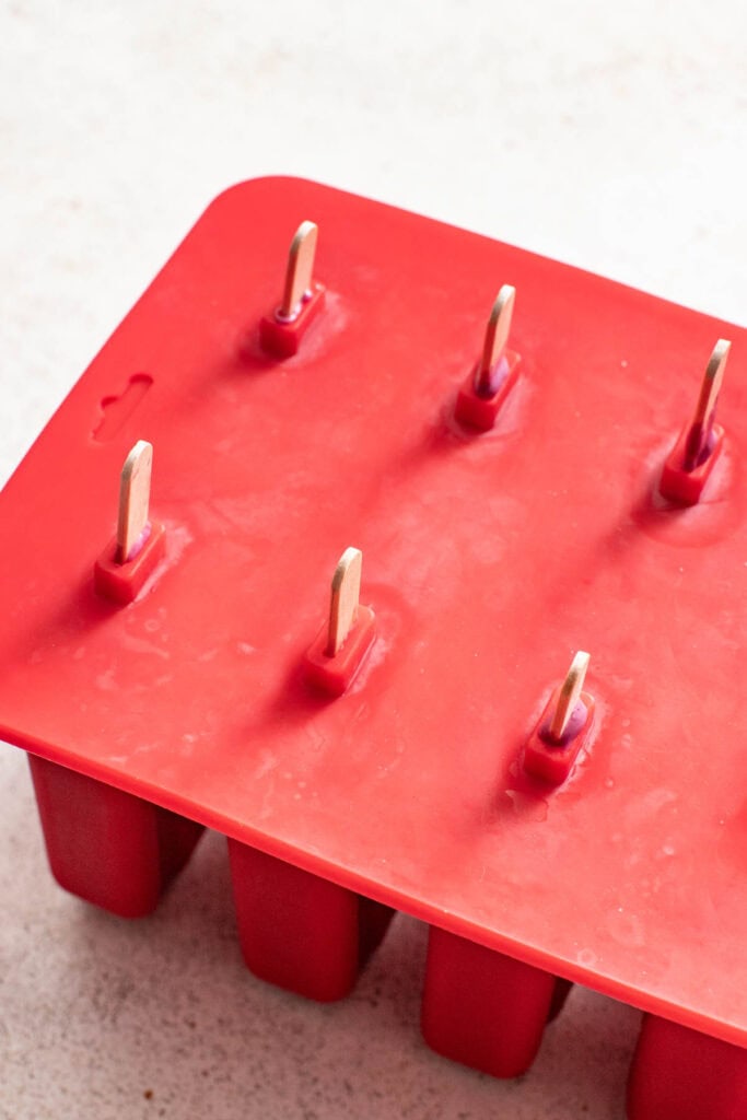 Placing the silicone popsicle lid on top of the popsicle molds.