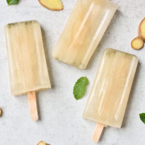 Three electrolyte popsicles on a white table with mint leaves and ginger.