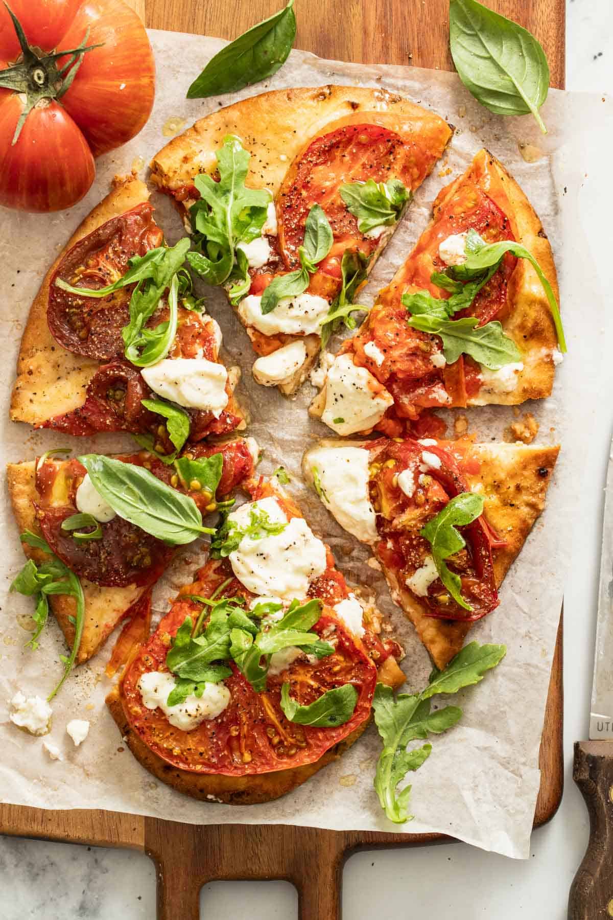 A whole naan pizza cut into slices with melted burrata cheese on top.