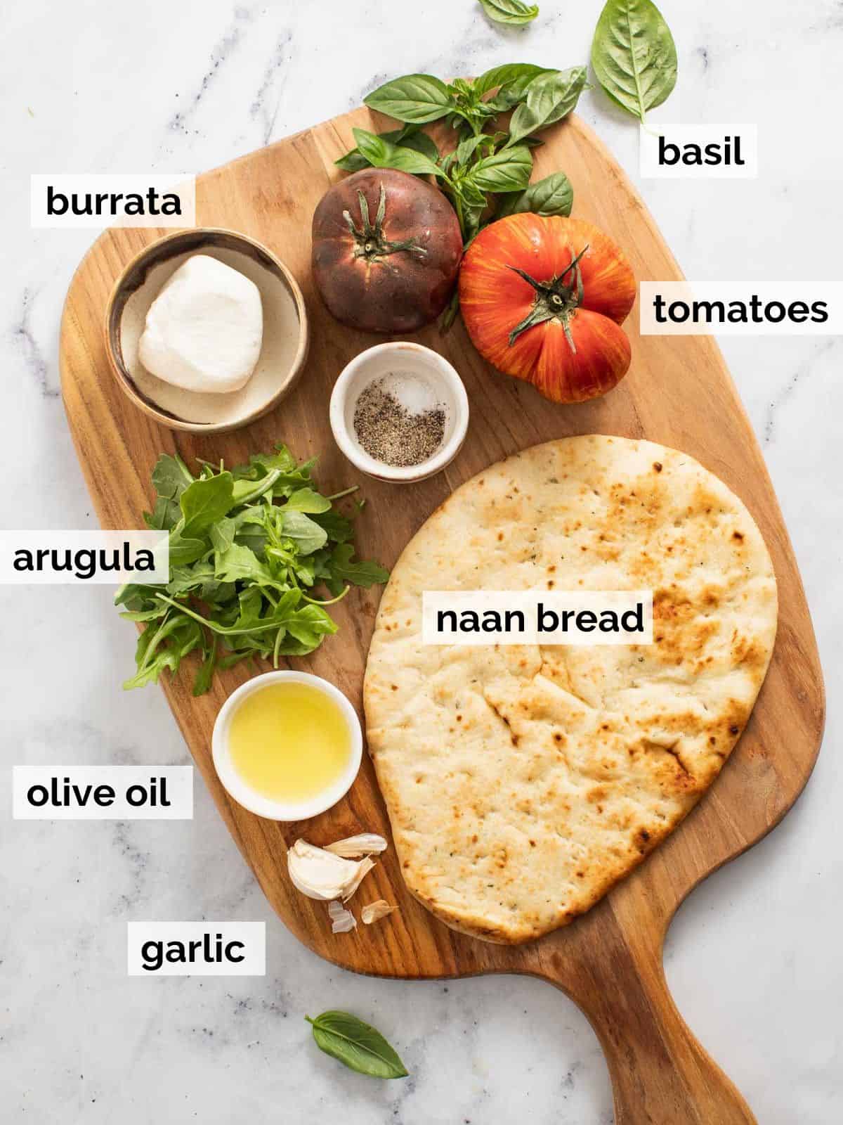 Ingredients for naan pizzas on a cutting board.