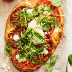 A burrata pizza made from naan bread that has a sprinkle of arugula and fresh basil on top.