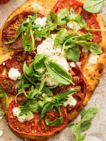 A burrata pizza made from naan bread that has a sprinkle of arugula and fresh basil on top.