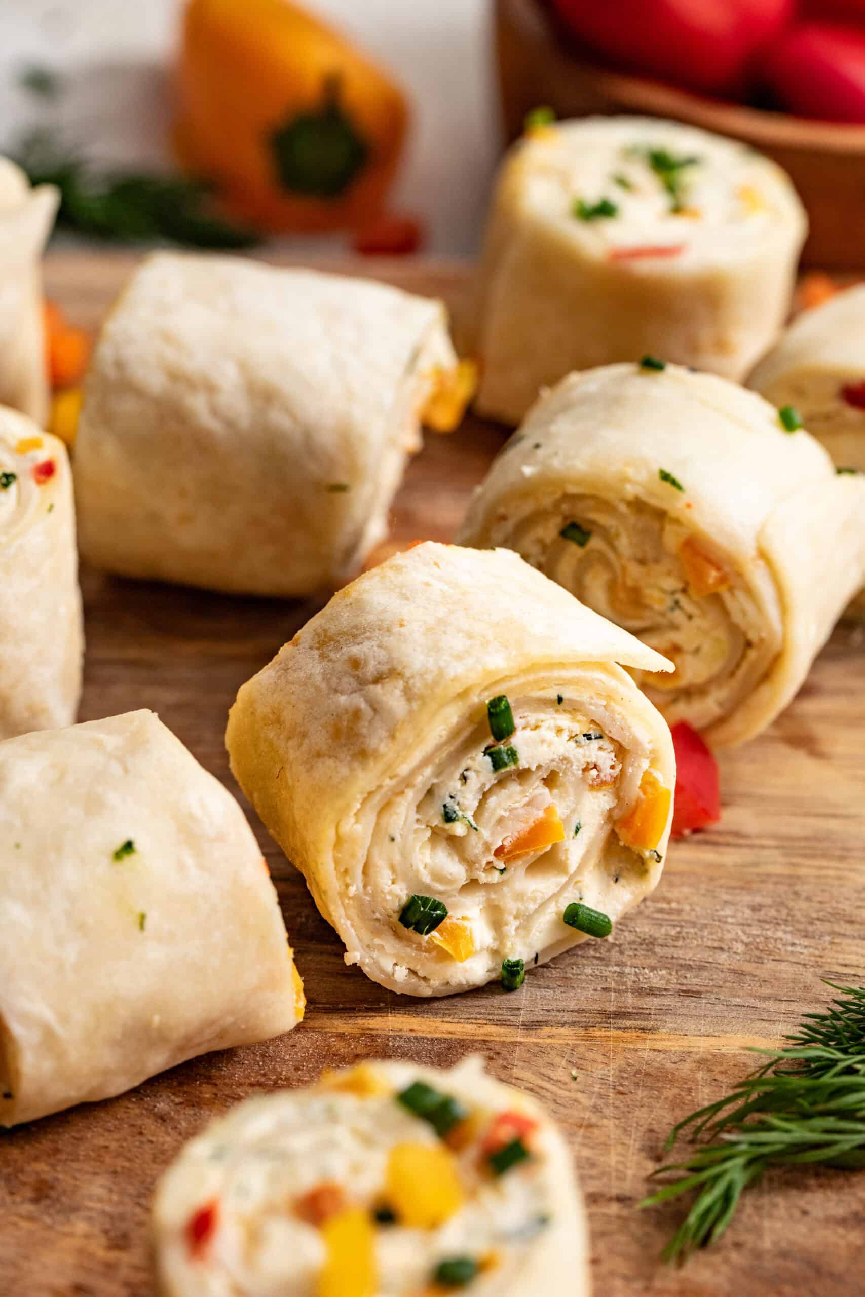 Tortilla roll ups on a cutting board, stuffed with peppers and cream cheese.