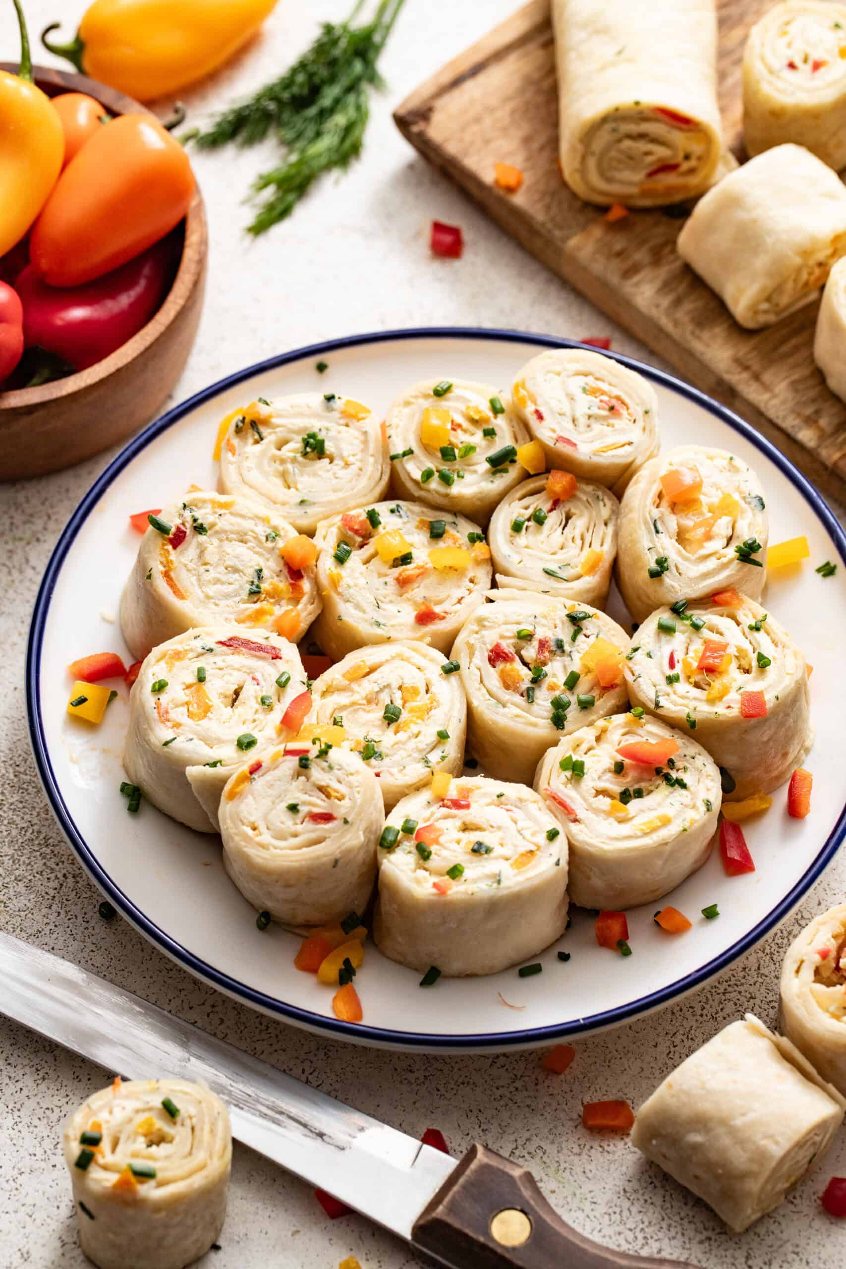 A plate of party pinwheels next to a cutting board with tortillas cut up and a knife.