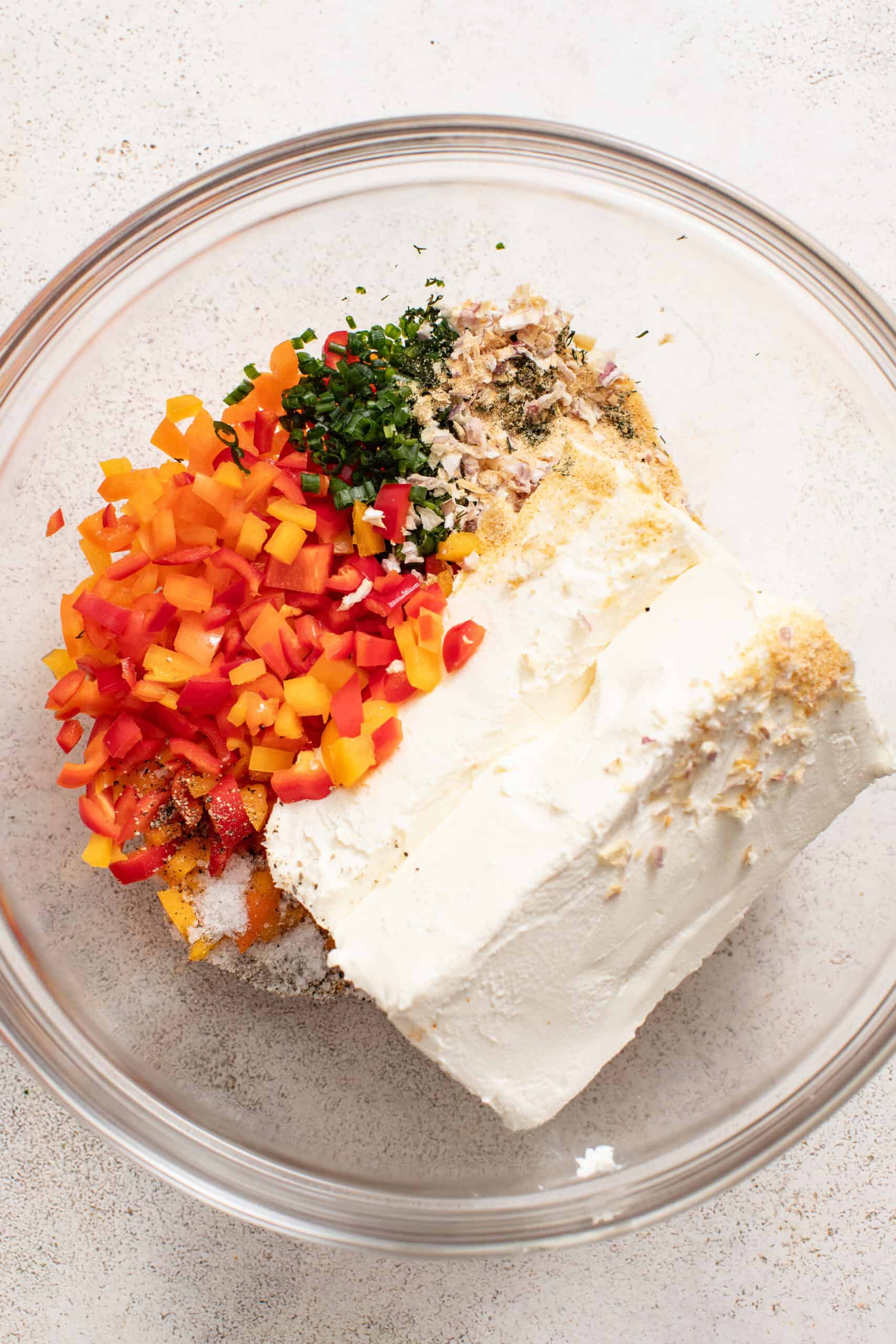 A bowl with chopped peppers, spices, and cream cheese.