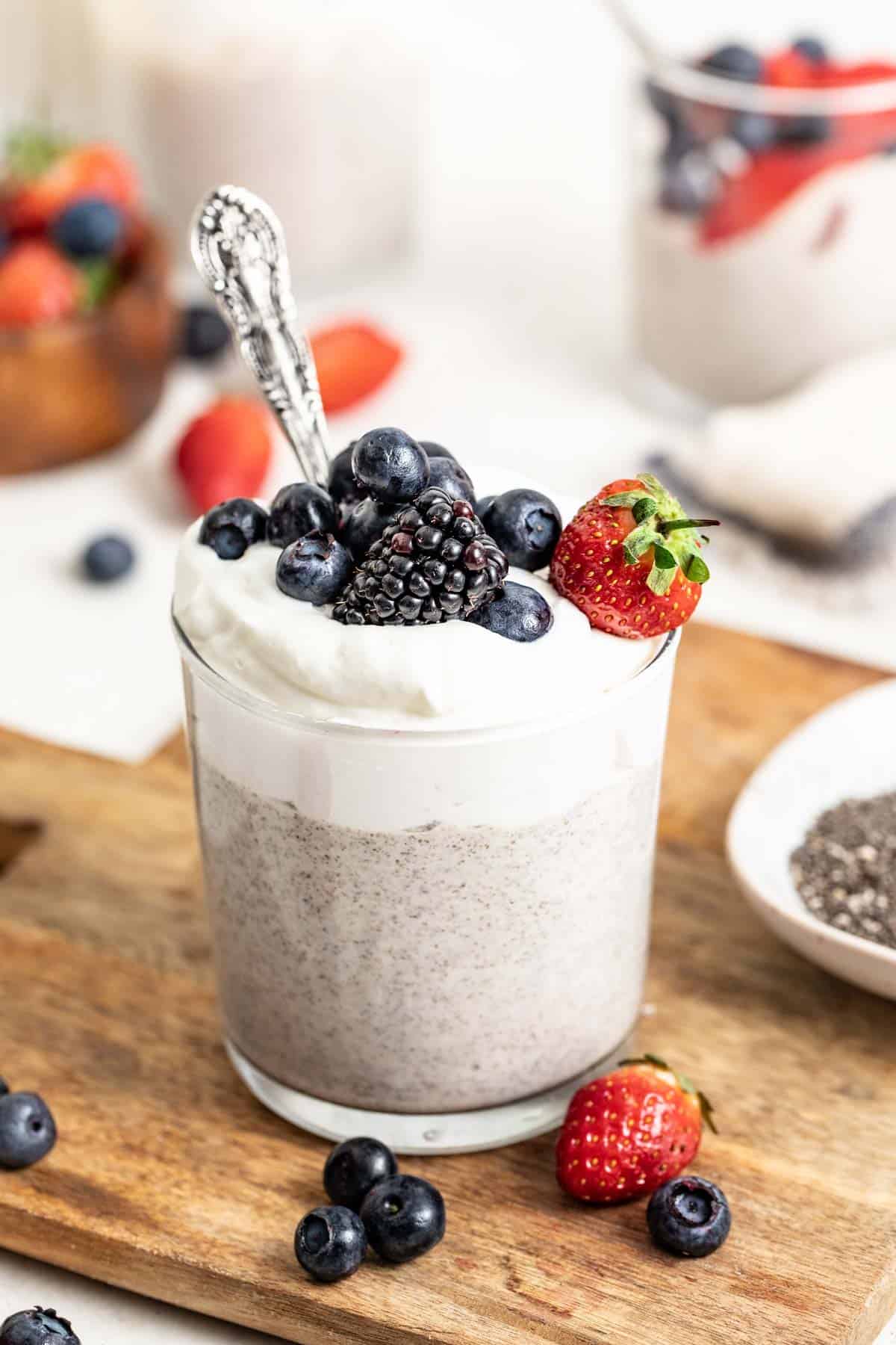 A whipped chia pudding on a wood board with a spoon dipped into it and assorted berries on top. 