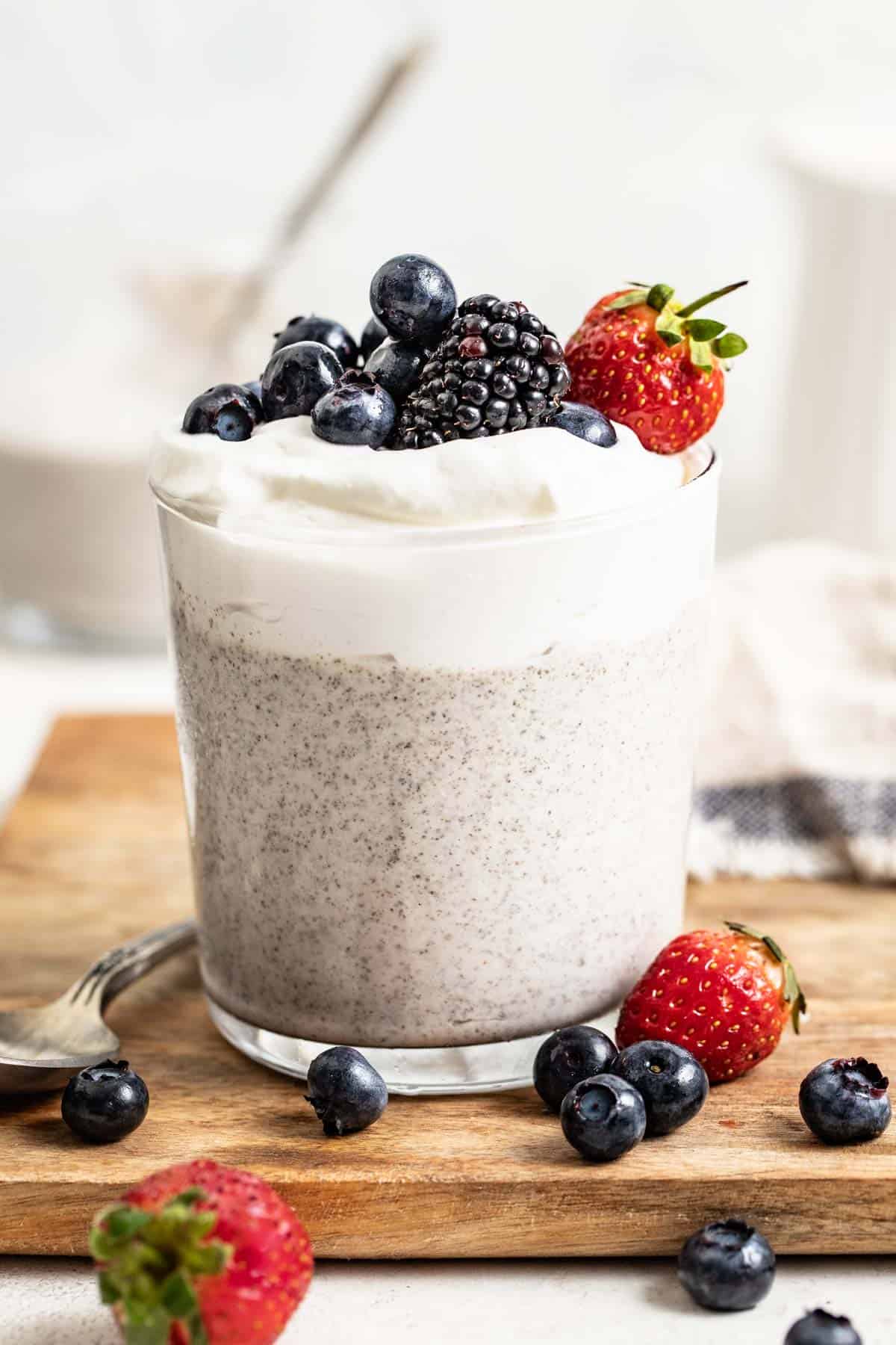 Blended chia pudding in a clear cup topped with whipped cream, blueberries, and blackberries.