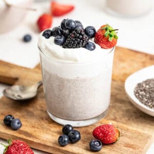 A cup filled with blended chia pudding topped with berries and whipped cream.