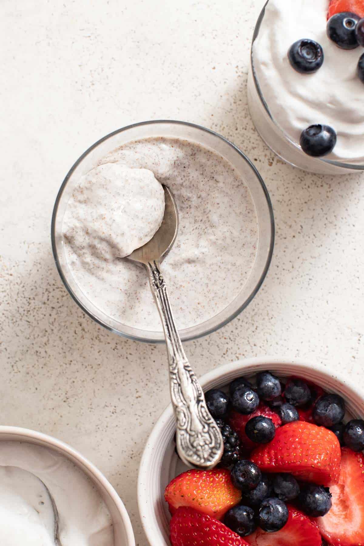 A spoon dipping into creamy chia pudding next to a bowl of berries.