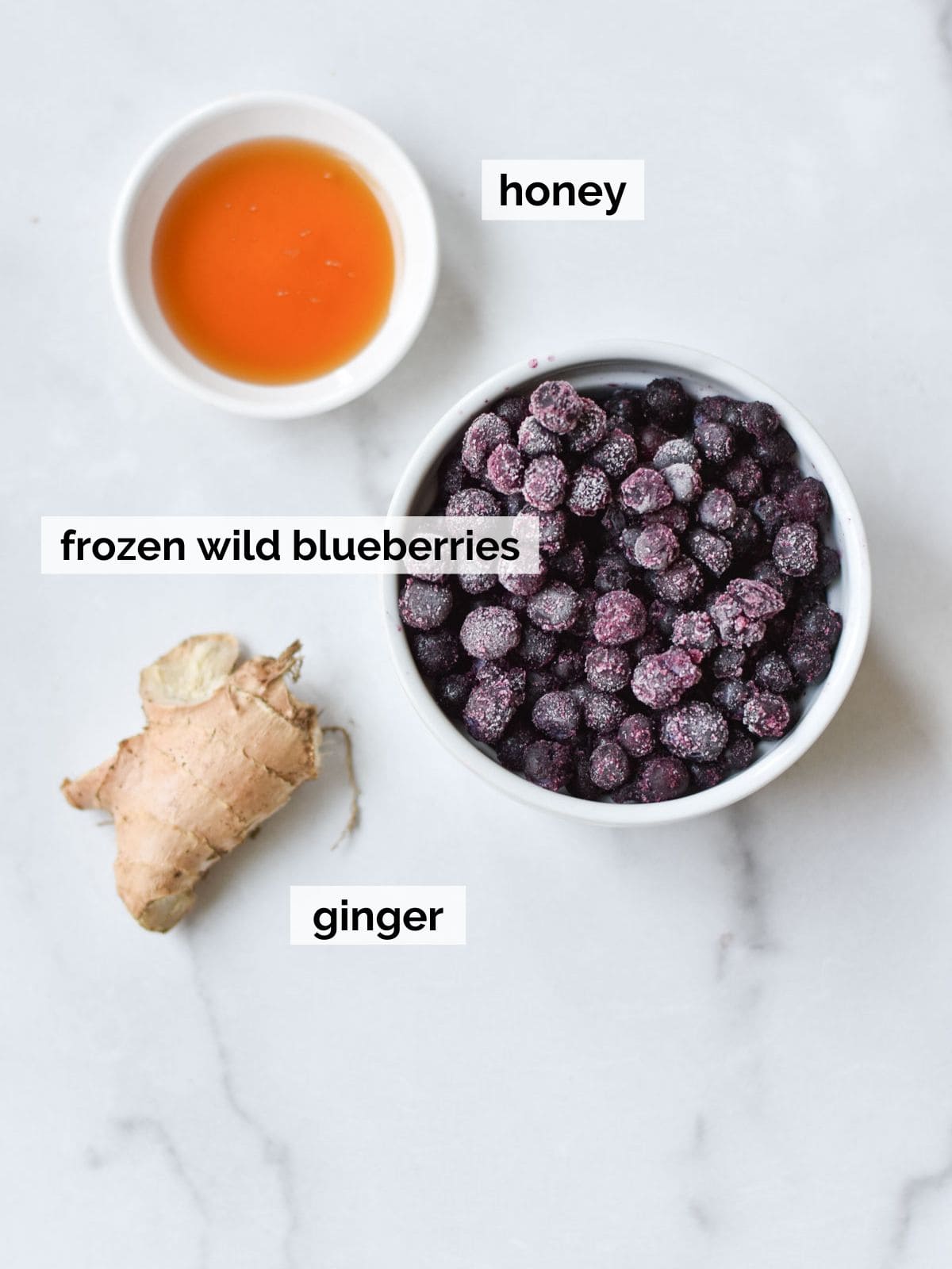 Ingredients for immunity shots that include blueberries and ginger on a white marble background.