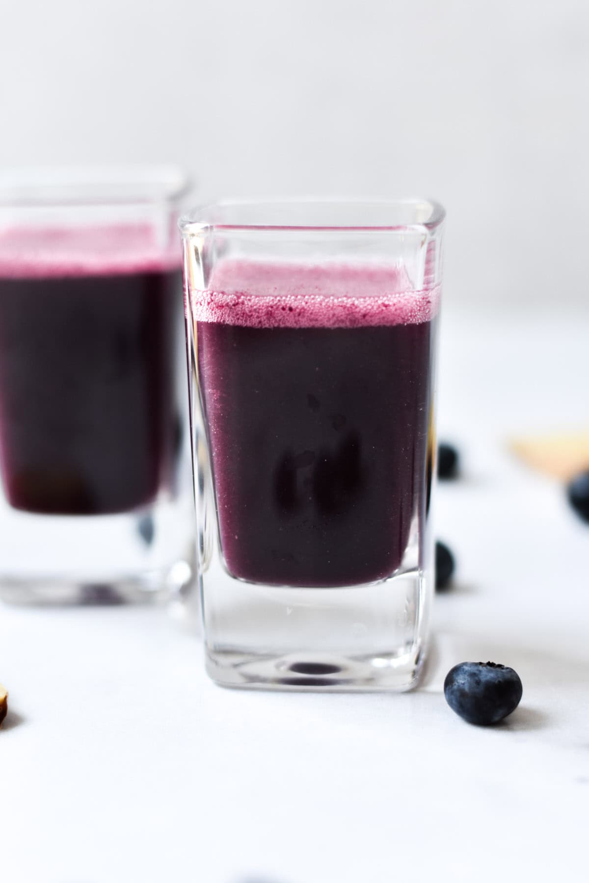 A shot glass with blueberry ginger immunity juice next to fresh blueberries.