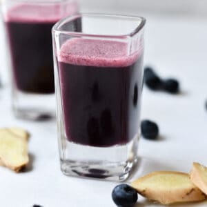 Immunity shots on a marble background with fresh ginger sliced next to the glasses.