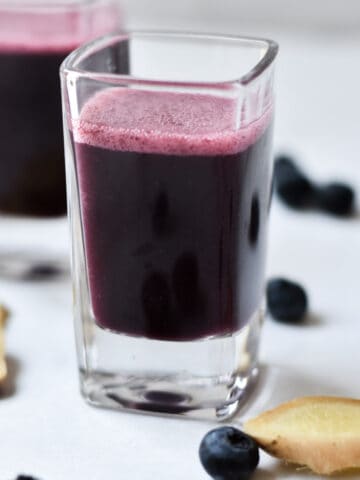 Immunity shots on a marble background with fresh ginger sliced next to the glasses.