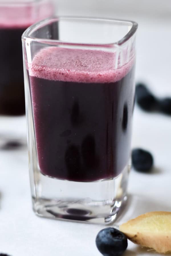 Immunity shots on a marble background with fresh ginger sliced next to the glasses.