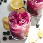 Two blueberry drinks surrounded by blueberries and ginger slices.