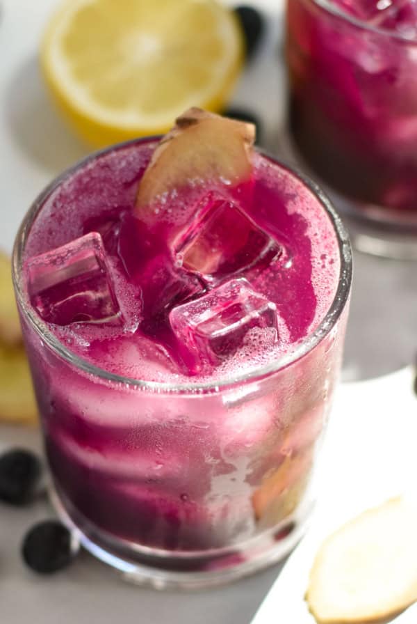 Two blueberry drinks surrounded by blueberries and ginger slices.