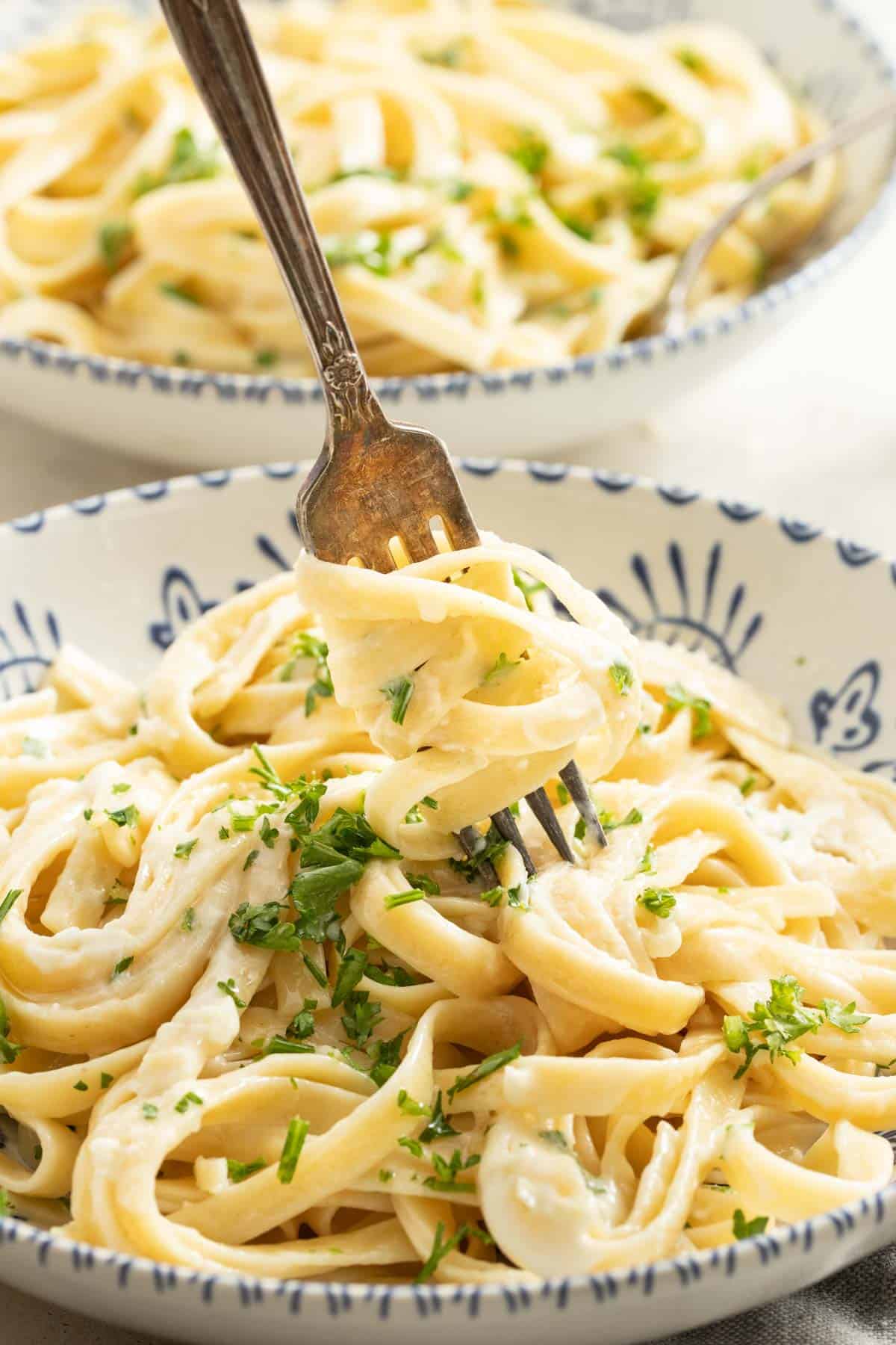 A fork dipping into a bowl of creamy boursin cheese pasta topped with parsley.