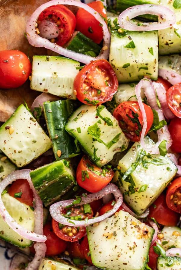 A wood spoon dipping into a bowl of mediterranean cucumber salad.