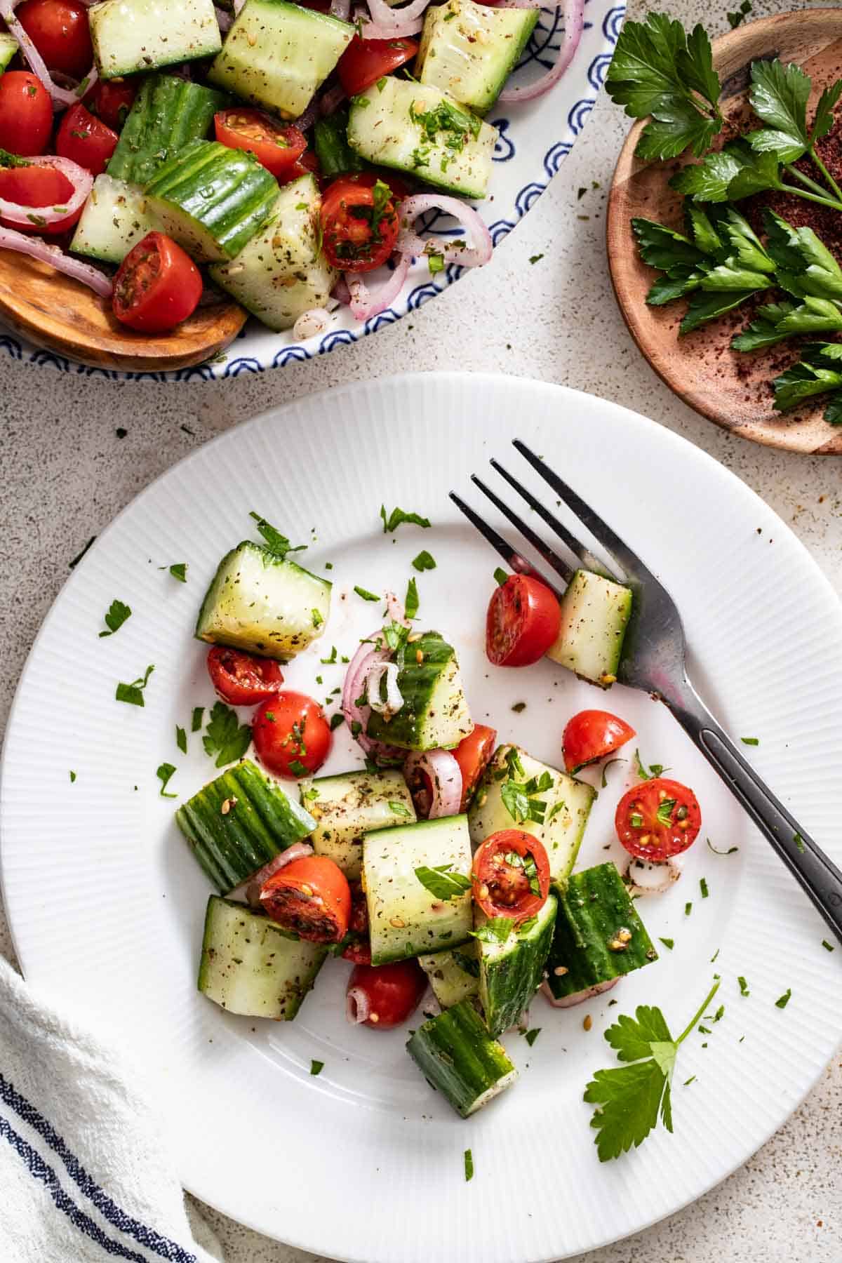 A white plate with a serving of cucumber salad next to a fork