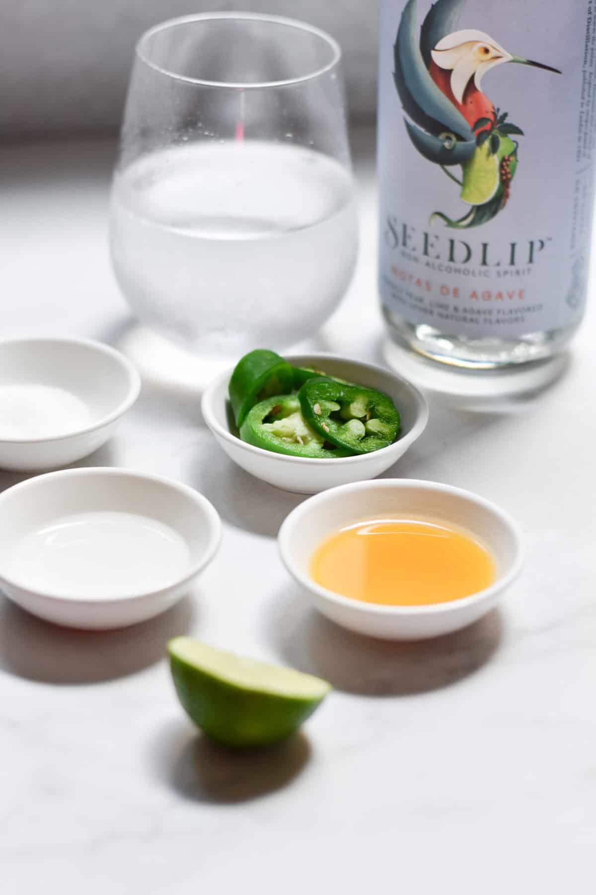 Small cups of ingredients next to a bottle of a tequila alternative.