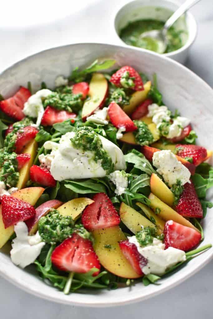 Mixed arugula, burrata, peaches, and basil in a white bowl.