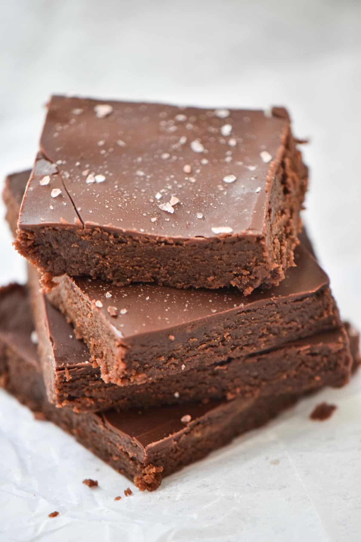 Stacked protein brownies topped with sea salt on a sheet of wax paper.