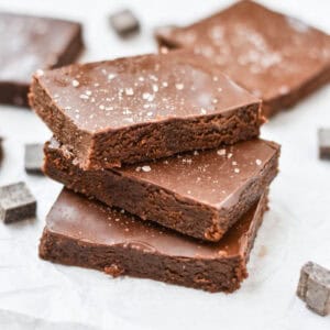 Stacked gooey brownies next to chocolate pieces.