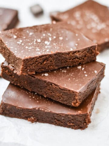 Stacked gooey brownies next to chocolate pieces.