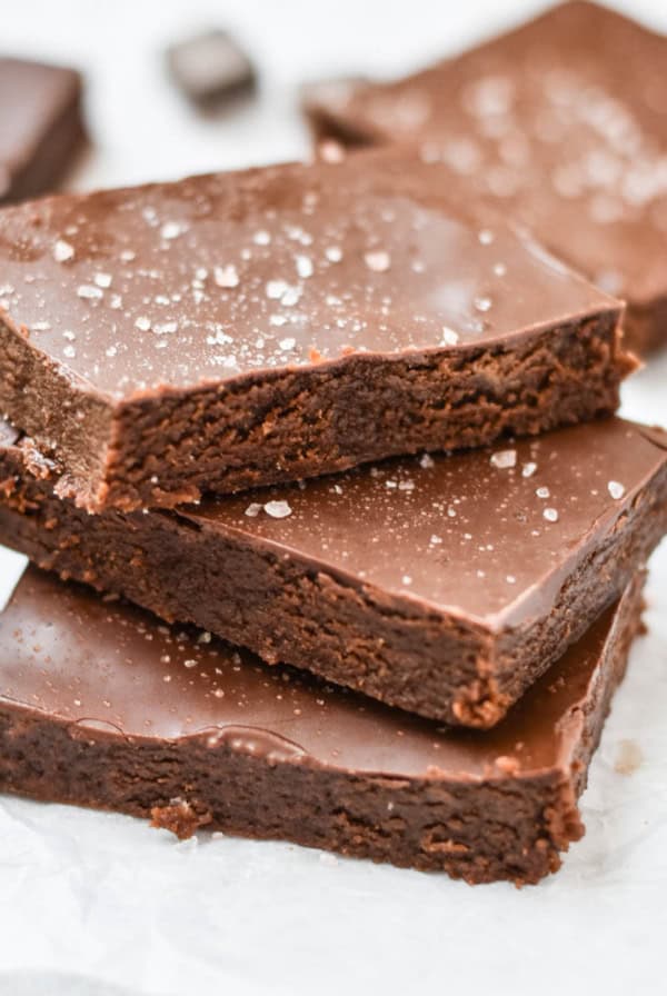Stacked gooey brownies next to chocolate pieces.