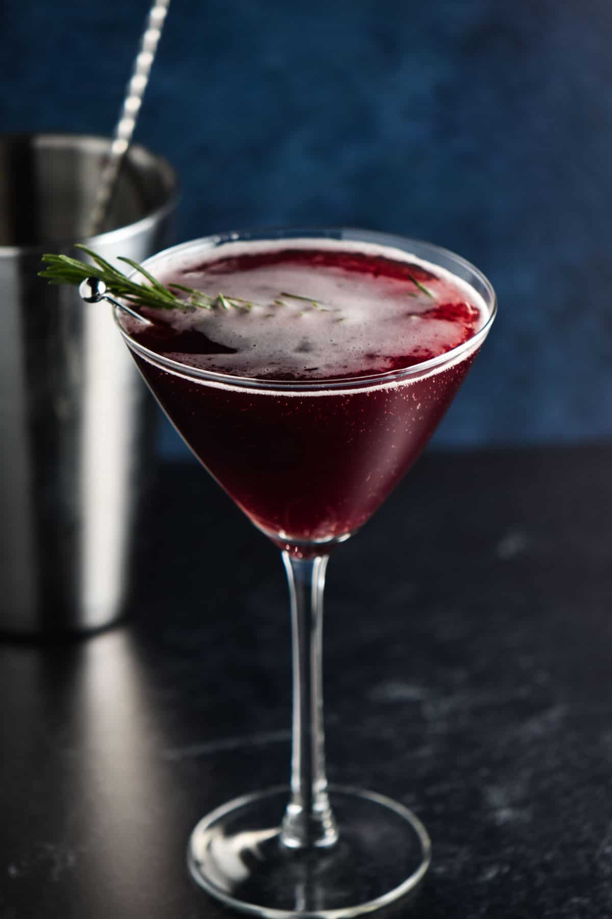 A martini glass with a tart cherry mocktail and a sprig of rosemary.